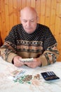 The grandfather in a sweater sits at the dacha at a table and counts money. Royalty Free Stock Photo