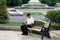 Grandfather in a white shirt and black pants is sitting on a bench.