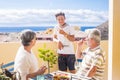 Grandfathers adult mature and teenager nephew enjoy outdoor in the terrace some leisure with food and drinks. ocean and city view