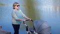 Grandma rolls stroller with newborn grandchild against lake