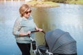 Grandma rolls stroller with newborn grandchild against lake