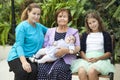 Grandmother with adult daughter and granddaughter sitting on bench with great-grandchild on her arms, family portrait Royalty Free Stock Photo