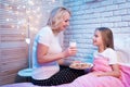 Grandmother brings granddaughter cookies and milk at night at home. Royalty Free Stock Photo