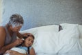 Grandmother checking body temperature of sick granddaughter in bed room Royalty Free Stock Photo