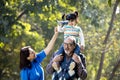 Grandmother with girl holding toy airplane sitting on grandfather`s shoulder at park