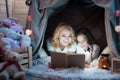 Grandmother and granddaughter are reading book in blanket house at night at home.