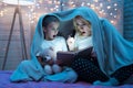 Grandmother and granddaughter are reading book with flashlight under blanket at night at home. Royalty Free Stock Photo