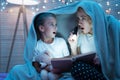 Grandmother and granddaughter are reading book with flashlight under blanket at night at home. Royalty Free Stock Photo