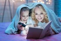 Grandmother and granddaughter are reading book with flashlight under blanket at night at home. Royalty Free Stock Photo