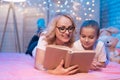 Grandmother and granddaughter are reading book before sleep at night at home. Royalty Free Stock Photo