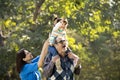 Grandmother with granddaughter sitting on grandfather`s shoulder at park