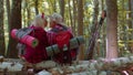 Grandmother grandfather senior tourists hikers sitting on tree and hugging, kissing in summer forest