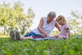 Grandmother with her grandaughter casually sitting on a blanket reading and talking in a park. Royalty Free Stock Photo