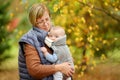 Grandmother with her infant grandson in a baby carrier having fun hiking in a forest on beautiful autumn day. Granny taking a walk Royalty Free Stock Photo