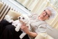 Grandmother holding small dog in her lap while relaxing on armchair at home Royalty Free Stock Photo