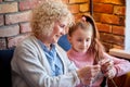 Grandmother Knitting Scarf WIth Grandgranddaughter In Living Room At Home