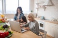 Grandmother with laptop and mom with daughter making breakfast.