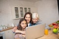 Grandmother, mother, daughter hugged at a laptop in the kitchen.