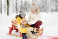 Grandmother / nanny / mother puts on a mitten to a small child during sledding in winter park