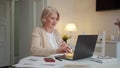 Grandmother puts on wireless headphones and turns on music from a laptop. She is very satisfied Royalty Free Stock Photo