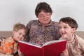 Grandmother reads a book for grandchildren. The children are laughing