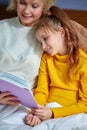 grandmother reads a book to little daughter lying on bed in children& x27;s room Royalty Free Stock Photo