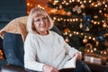 Grandmother sitting on the chair with book in festive New year room with christmas decorations Royalty Free Stock Photo