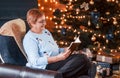 Grandmother sitting on the chair with book in festive New year room with christmas decorations Royalty Free Stock Photo