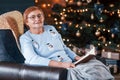 Grandmother sitting on the chair with book in festive New year room with christmas decorations Royalty Free Stock Photo