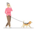 The grandmother in a sports pink sweater and brown pants walks with the dog talking on the phone.