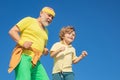 Grandpa and grandson exercising on blue sky. Cheerful grandpa and cute child grandson jogging in sportswear on sky Royalty Free Stock Photo