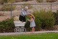 Grandpa helping little girl with hat on walk with toy buggy Royalty Free Stock Photo