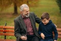 Grandpa and his grandson spend time together in the park. They are sitting on the bench. Walking in the park and Royalty Free Stock Photo