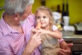 Grandpa holding in arms his granddaughter in his lap, sitting in the kitchen, smiling, enjoying