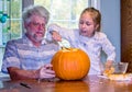 Grandpa watches as girl scoops out a pumpkin