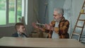 Grandpa is telling and teaching his grandson how the water level works. An elderly man and a young guy are sitting in an