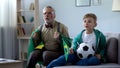 Grandpa wrapped in Brazil flag watching football with boy, worrying about game Royalty Free Stock Photo