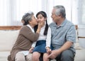 Happy asian grandparents sitting on sofa at home playing and kiss on cheek of little granddaughter Royalty Free Stock Photo