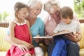 Grandparents And Grandchildren Reading Book On Garden Seat Royalty Free Stock Photo