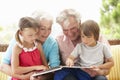 Grandparents And Grandchildren Reading Book On Garden Seat Royalty Free Stock Photo