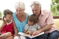 Grandparents And Grandchildren Reading Book On Garden Seat