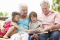 Grandparents And Grandchildren Reading Book On Garden Seat