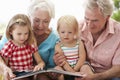 Grandparents And Grandchildren Reading Book On Garden Seat Royalty Free Stock Photo