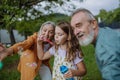 Grandparents and granddaughter are blowing bubbles from a bubble wand, having fun outdoors in the garden during warm Royalty Free Stock Photo