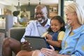 Grandparents And Granddaughter With Digital Tablet Sitting On Sofa At Home Together Royalty Free Stock Photo