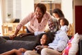 Grandparents With Granddaughter Sitting On Sofa At Home Watching Movie With Family In Background Royalty Free Stock Photo