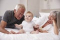 Grandparents Lying In Bed At Home Looking After Baby Grandson Royalty Free Stock Photo