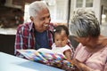 Grandparents Reading Book With Baby Granddaughter At Home