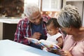 Grandparents Reading Book With Baby Granddaughter At Home