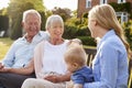 Grandparents Sit Outdoors With Baby Grandson And Adult Daughter